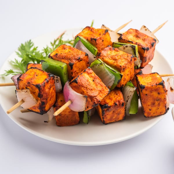 Grilled paneer tikka skewers with bell peppers and onions, garnished with cilantro on a white plate.