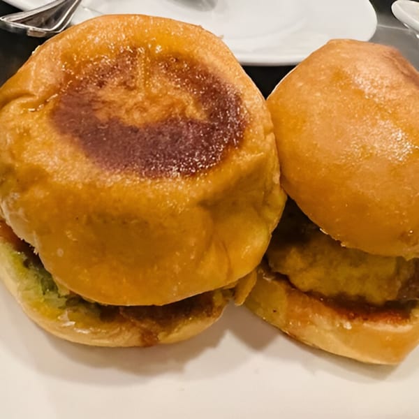 Two golden-brown Indian vada pavs with green chutney and red sauce on a white plate.