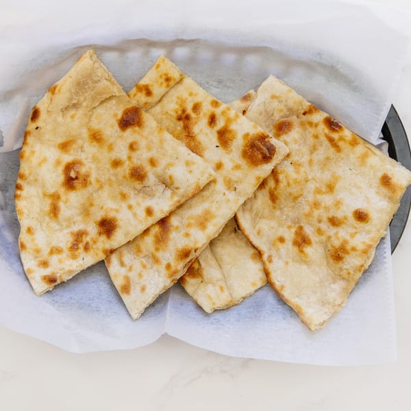 Golden brown Indian flatbread, likely naan or roti, cut into triangles and served in a basket.