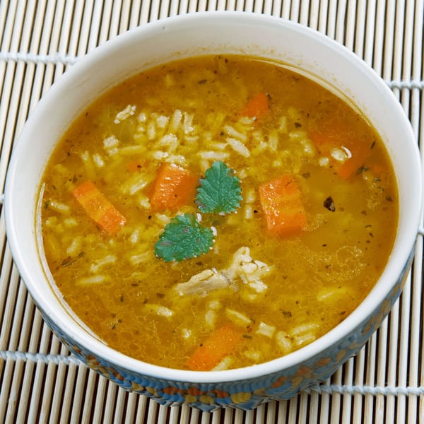 Close-up of a bowl of Indian vegetarian soup with rice, carrots, and herbs.
