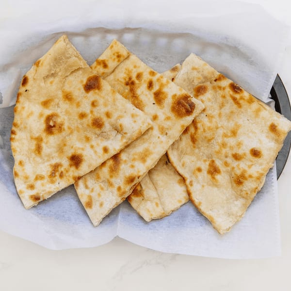 Four pieces of golden-brown Indian naan bread, folded and served in a basket lined with white paper.