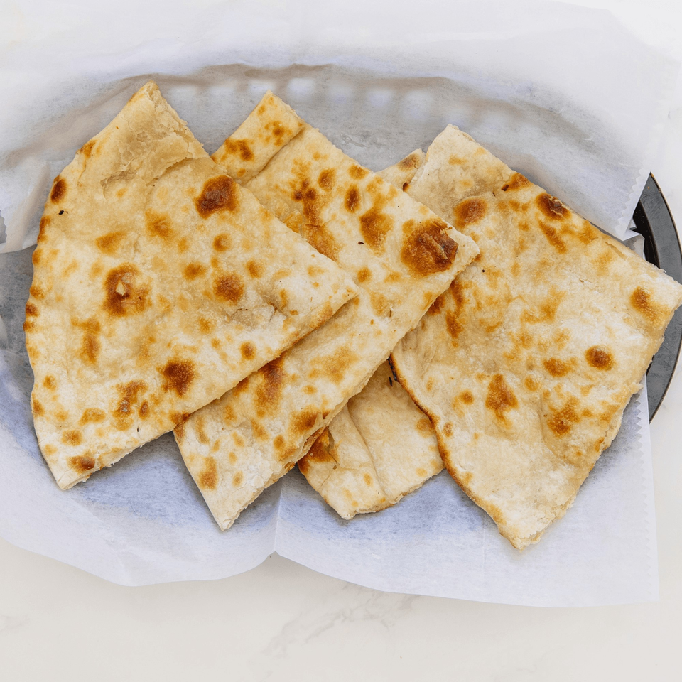 Four pieces of golden-brown Indian naan bread, folded and served in a basket lined with white paper.