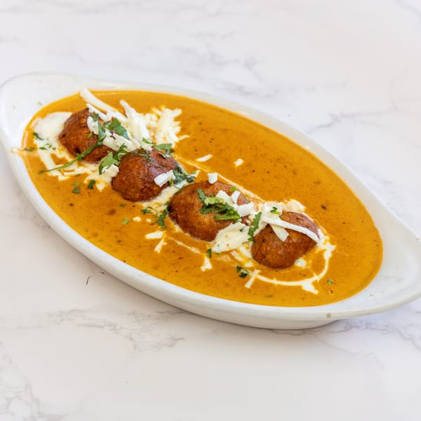 Three Indian vegetarian kofta balls in a rich orange curry sauce, garnished with cream, cheese, and herbs.