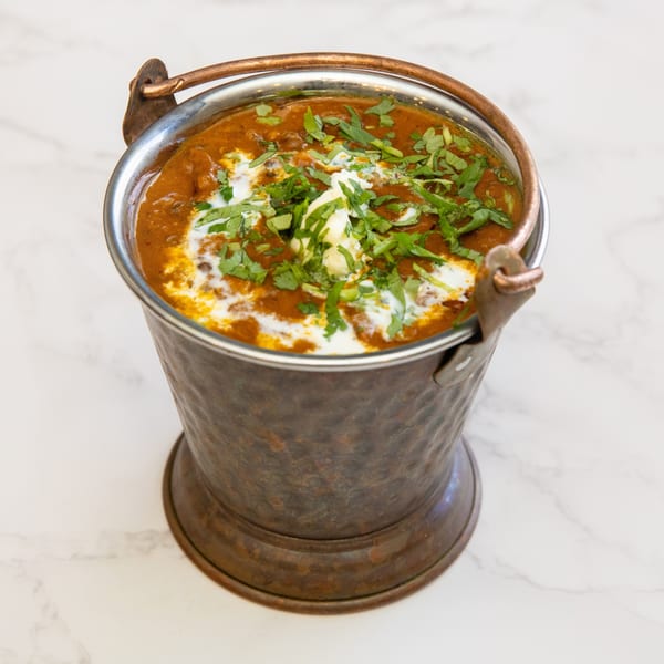 Dal Makhani, an Indian lentil dish, served in a rustic copper bucket, garnished with cream and cilantro.
